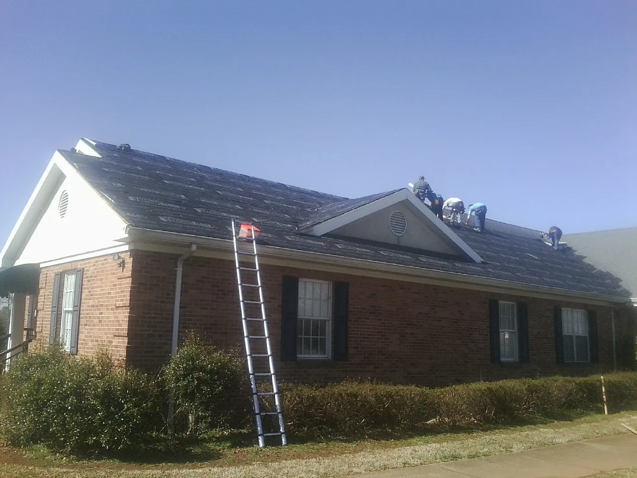 Crew tearing shingles off a brick ranch roof with a ladder set — Emergency Roof Repair work by our crew in East Providence