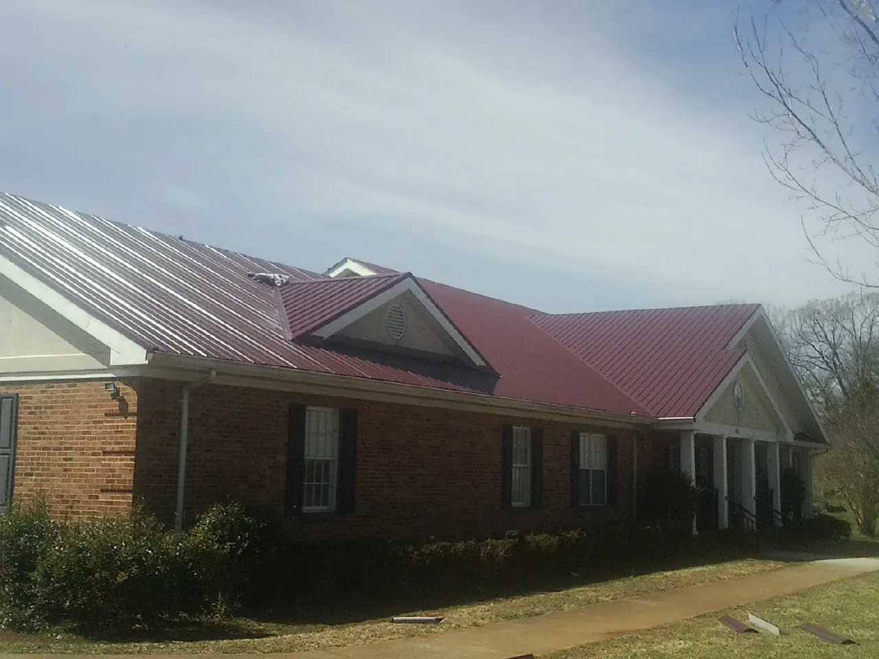 Red metal roof with gabled entries on a long brick building, from a Hail Damage Roof Repair job in East Providence
