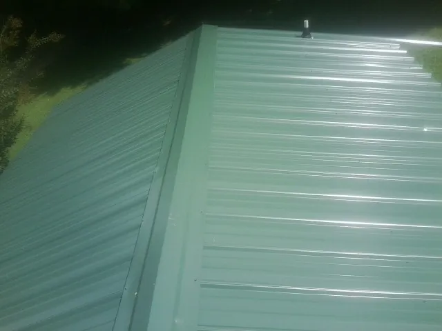 New green metal panels meeting at the ridge of a roof — Flat Roof Repair work by our crew in East Providence