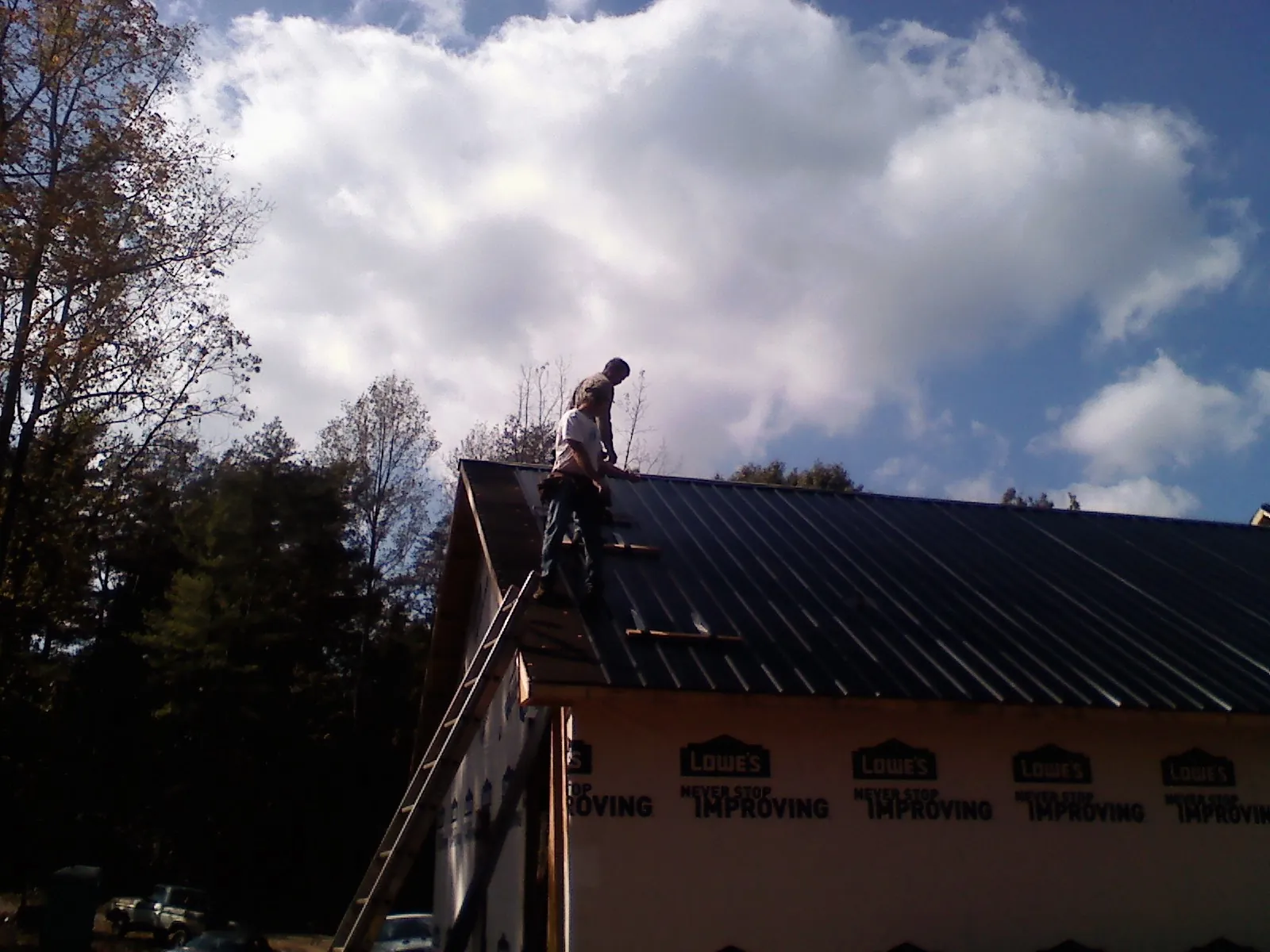 Roofer fastening dark metal panels high against a cloudy sky, from a Roof Inspection job in East Providence