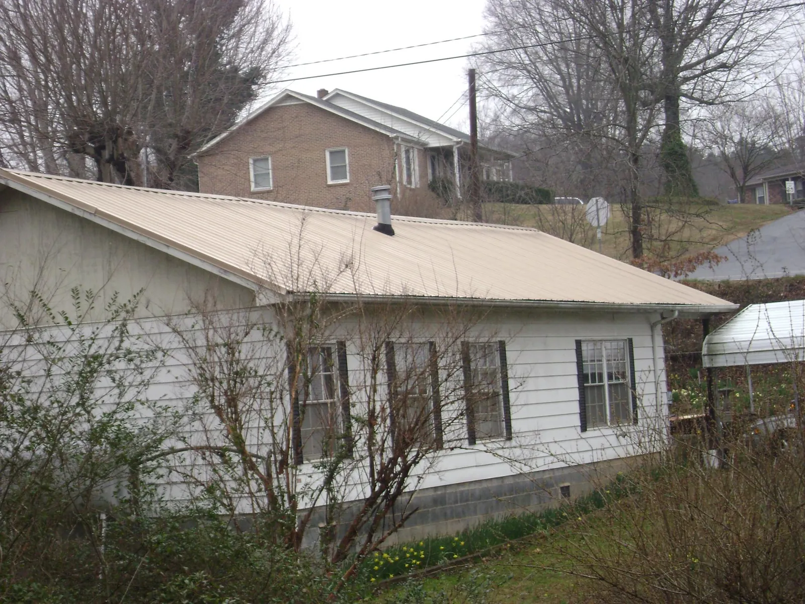 Tan metal roof on a white sided house set into a hillside — Commercial Roofing by Roofing Brothers in East Providence
